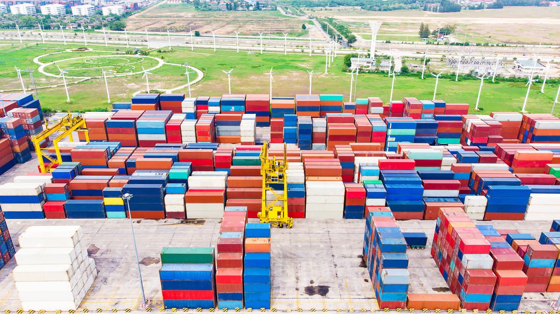 Vue aérienne d’un parc de containers high cube empilés, de différentes couleurs, utilisés pour le stockage et le transport maritime, avec grue de manutention au centre du terminal.