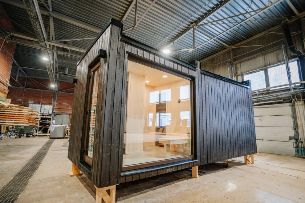 Espace de vie aménagé dans un container, avec bardage bois sombre et grande baie vitrée, en cours de construction dans un atelier pour créer un habitat container moderne et confortable.