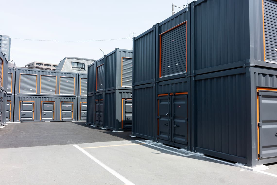 Parc de containers d’occasion empilés, équipés de portes roulantes et utilisés comme espaces de stockage, illustrant une solution rentable pour investir dans les containers d’occasion.